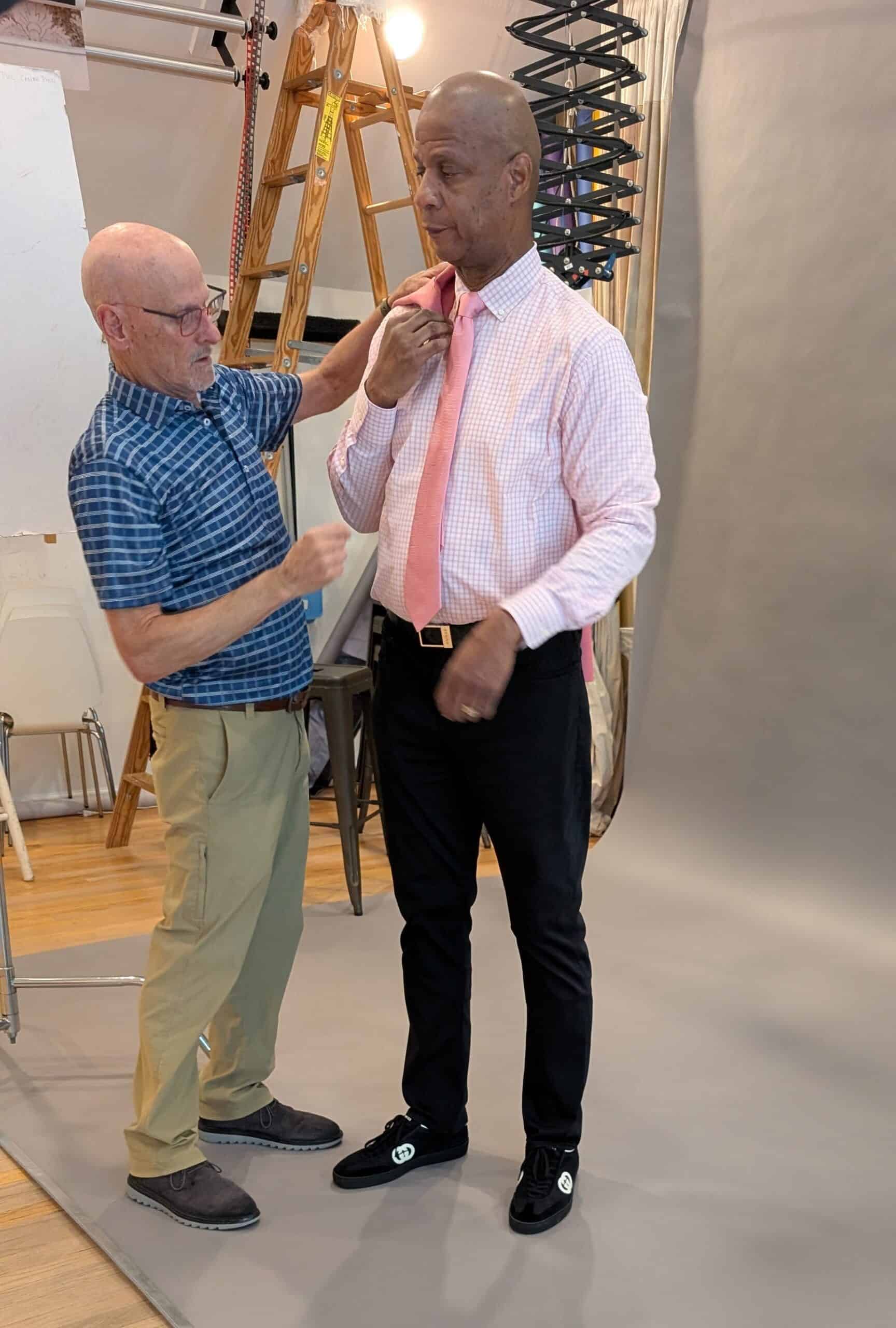 Photographer adjusting model's tie during photoshoot in studio.